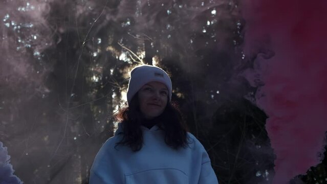 a girl holds a burning smoke bomb of red and blue colors in her hands while in the forest, slow motion