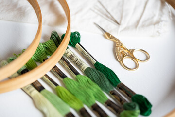 madejas de hilo para bordar en colores verdes con bastidor o aro de madera, tijeras y agujas  