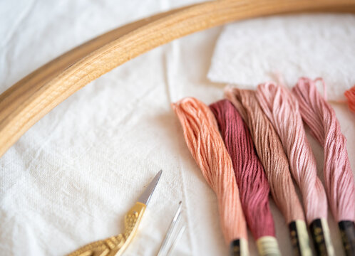 madejas de hilo para bordar en colores rosa con bastidor o aro de madera, tijeras y agujas  