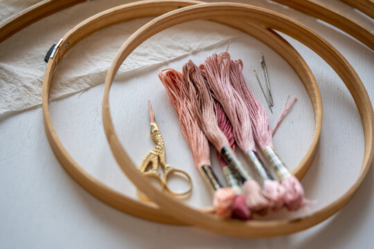 madejas de hilo para bordar en colores rosa con bastidor o aro de madera, tijeras y agujas  