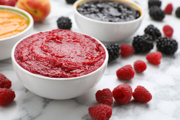 Different puree in bowls and fresh ingredients on white marble table, closeup