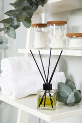 Aromatic reed air freshener, toiletries and rolled towels on white wooden shelf in bathroom