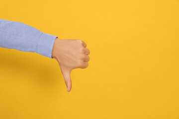 Fototapeta premium Man showing thumb down on orange background, closeup. Space for text