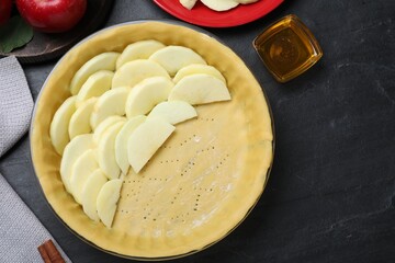 Flat lay composition with dish of fresh apple slices and raw dough on black table. Baking pie