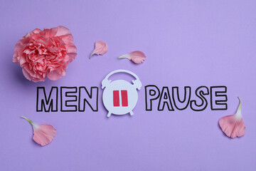 Word Menopause with paper alarm clock and pink carnation flower on violet background, flat lay