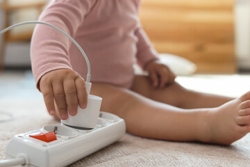 Cute baby playing with charger and power strip on floor at home, closeup. Dangerous situation