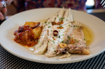Eating in restaurant of fresh grilled on old charcoal parrillas sea bass fish in small fisherman's village Getaria, Basque Country, Spain