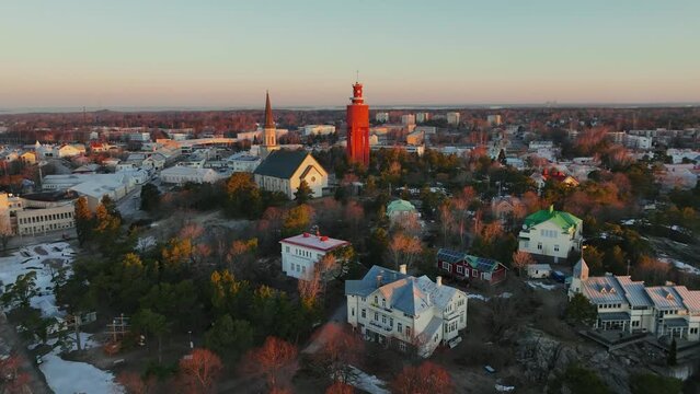 Aerial view away from the water tower and church, over the city of Hanko, sunset in Uusimaa, Finland - rotating, pull back, drone shot