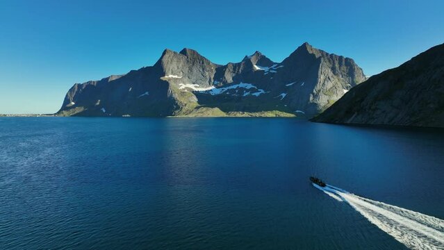 RIB boat tour driving in middle of steep mountains, in sunny Lofoten, Norway - Aerial view