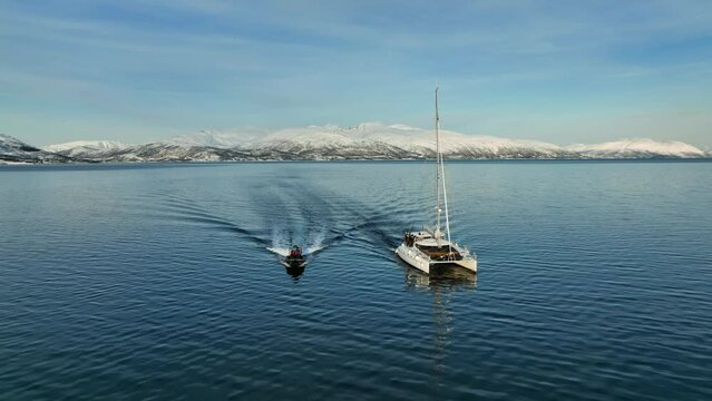 Aerial view in front of RIB boat and sailboat driving in snowy Norway - pull back, drone shot
