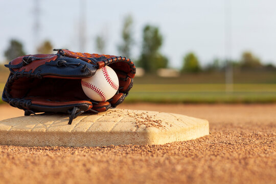 Selective focus of a baseball in a leather mitt on a base of a baseball park infield on a sunny afternoon