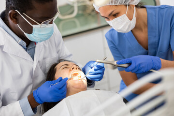 African-american man dentist and asian woman assistant doing tooth restoration for female patient.