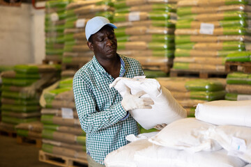 African-american man working in warehouse, lifting heavy bag. Storehouse worker carrying bag.
