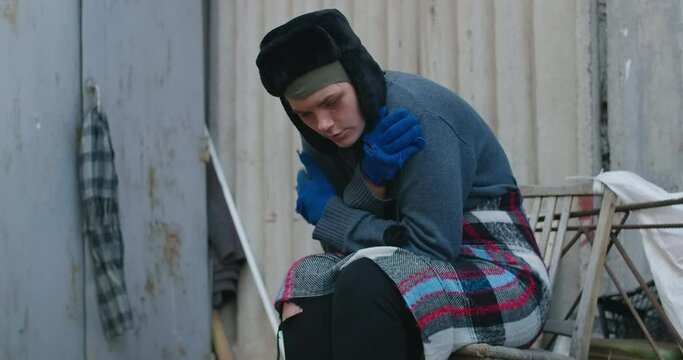 Side view of Caucasian homeless young woman shivering sitting on urban city street. Portrait of desperate frustrated person outdoors shaking in slow motion. Cinema 4k ProRes HQ