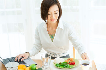Obraz na płótnie Canvas パソコンを見ながら朝食をとる女性