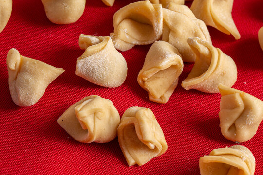 Traditional Italian capeletti .(tortellini, agnolini) fresh pasta stuffed with chicken, especially for preparing soup on cold nights. Fresh pasta on table with red tablecloth
