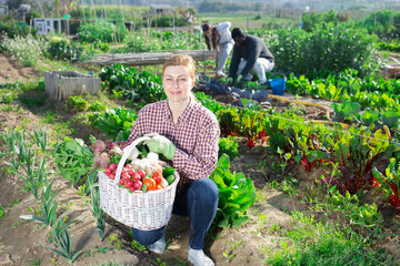 Portrait of a smiling young woman in the vegetable garden with a basket of harvested crops