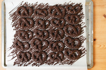 Baking sheet tray of Schokobrezeln, German Christmas cookies made from cocoa shortcrust dough in Pretzel form decorated with melted, tempered semi-sweet chocolate drizzle on wooden table - 530702587