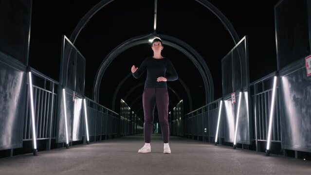 woman is dancing like robot in dark tunnel in night city, flashmob of modern street dancers