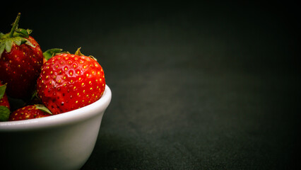 Fresh ripe delicious strawberries in a white bowl on a black background