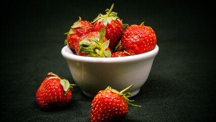 Fresh ripe delicious strawberries in a white bowl on a black background