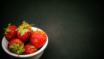 Fresh ripe delicious strawberries in a white bowl on a black background