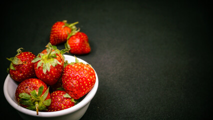 Fresh ripe delicious strawberries in a white bowl on a black background