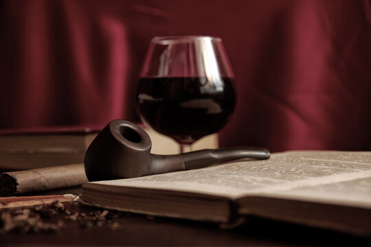 Dark velvet purple image with smoking pipe, tobacco, book and brandy. Old man's room for evening leisure activity