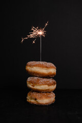 Traditional German or Austrian doughnut served for carnival or New Year's Eve filled with rose hip jam and dusted with cinnamon and sugar with sparkler on black background - 530706179