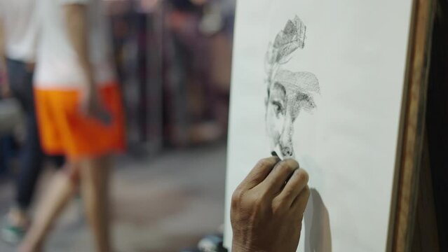 At the side of Chiang Mai, Thailand's market, a sketch artist uses charcoal to sketch the face of a beautiful Asian woman.