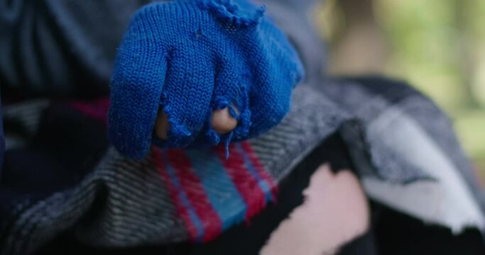 Close-up hand of unrecognizable homeless person in blue torn gloves. Caucasian young woman in urban park. Cinema 4k ProRes HQ