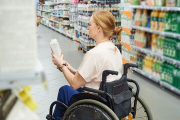 Obraz premium Profile of a female customer shopping for groceries in a supermarket, while sitting in a wheelchair