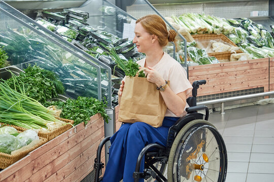 woman in a supermarket chooses vegetables, herbs, uses an eco-friendly bag, sitting in a wheelchair