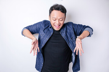 Shocked Asian man wearing blue navy shirt pointing at the copy space down below him, isolated by...