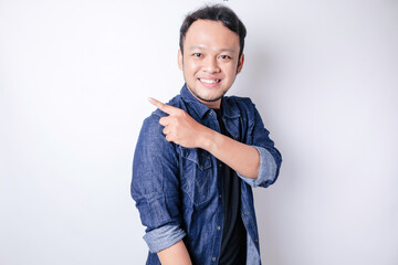 Smiling handsome Asian man pointing finger sideward to empty space isolated white background