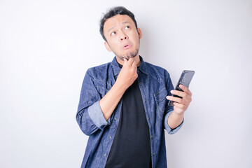 Portrait of a thoughtful young Asian man wearing navy blue shirt looking aside while holding smartphone