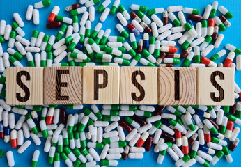 Multicolored pills and wooden block with inscription SEPSIS