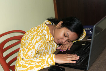 Stressed young Indian business woman sleeping on his laptop in his office desk. Working woman, night shift work load concept. Selective focus.