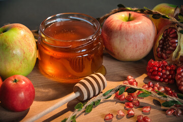 Red and green apples, pomegranate and honey in a glass jar on wooden background. Traditional Jewish new year food. Happy Rosh Hashanah concept.