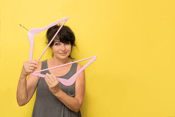 pretty woman playfully holding clothes hangers on yellow background with copy space