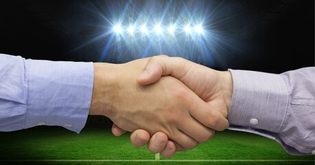 Composition of two businessmen shaking hands over sports stadium