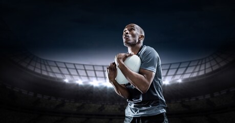 Composition of male rugby player holding rugby ball over sports stadium