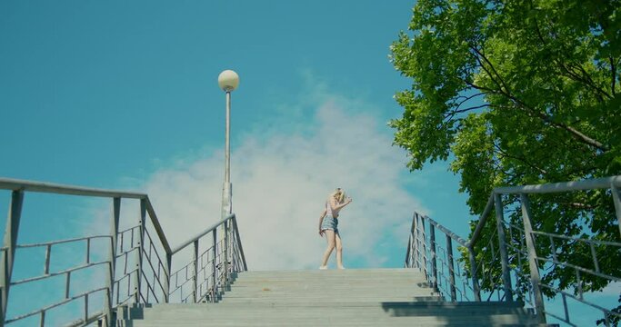 A stylish girl is dancing the shuffle dance at the top of the stairway, the general plan, the background is blue sky.