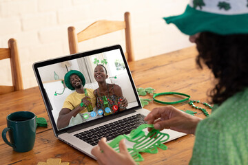 Mixed race woman in costume making st patrick's day video call to smiling couple on laptop at home - Powered by Adobe