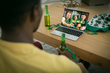 African american man holding beer making st patrick's day video call to friends on laptop at home