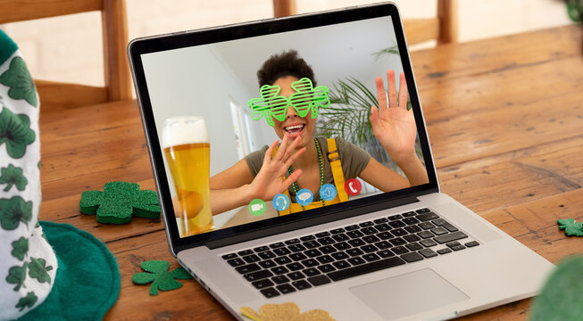 Mixed race woman having st patrick's day video call smiling and waving on laptop screen at home