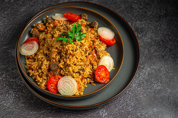 Pilaf, a dish of meat , rice, carrot with spices with dried fruit and almonds, and scented with cumin, cinnamon and turmeric. On a grey plate on a grey background. Estern cuisine