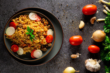 Pilaf, a dish of meat , rice, carrot with spices with dried fruit and almonds, and scented with cumin, cinnamon and turmeric. On a grey plate on a grey background. Estern cuisine