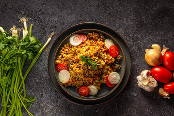 Pilaf, a dish of meat , rice, carrot with spices with dried fruit and almonds, and scented with cumin, cinnamon and turmeric. On a grey plate on a grey background. Estern cuisine