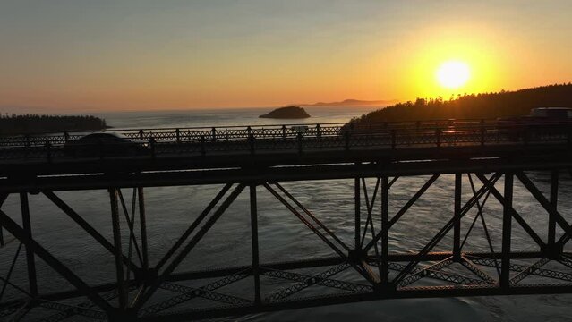 Drone shot of vehicles driving through the glow of the sun at sunset on Deception Pass.